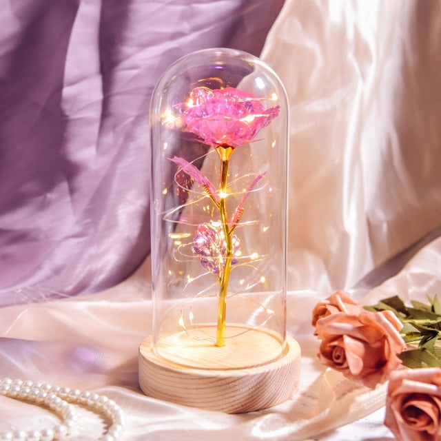 Artificial galaxy rose flowers in glass dome with LED lighting on black wood base, perfect for home decor or romantic gift for Valentine's Day, weddings. or any special occasion.